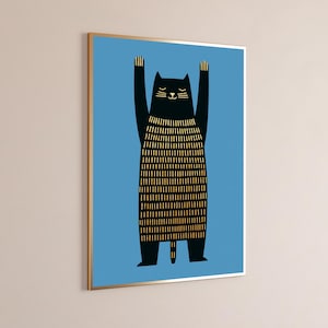 Op de afbeelding: Een ingelijste muurkunstprint met een zwarte kat met opgeheven armen tegen een effen blauwe achtergrond. De kat heeft een goudkleurig lichaam met verticale streepjes en een eenvoudig gouden gezicht. De lijst is dun en heeft een metaalkleur.