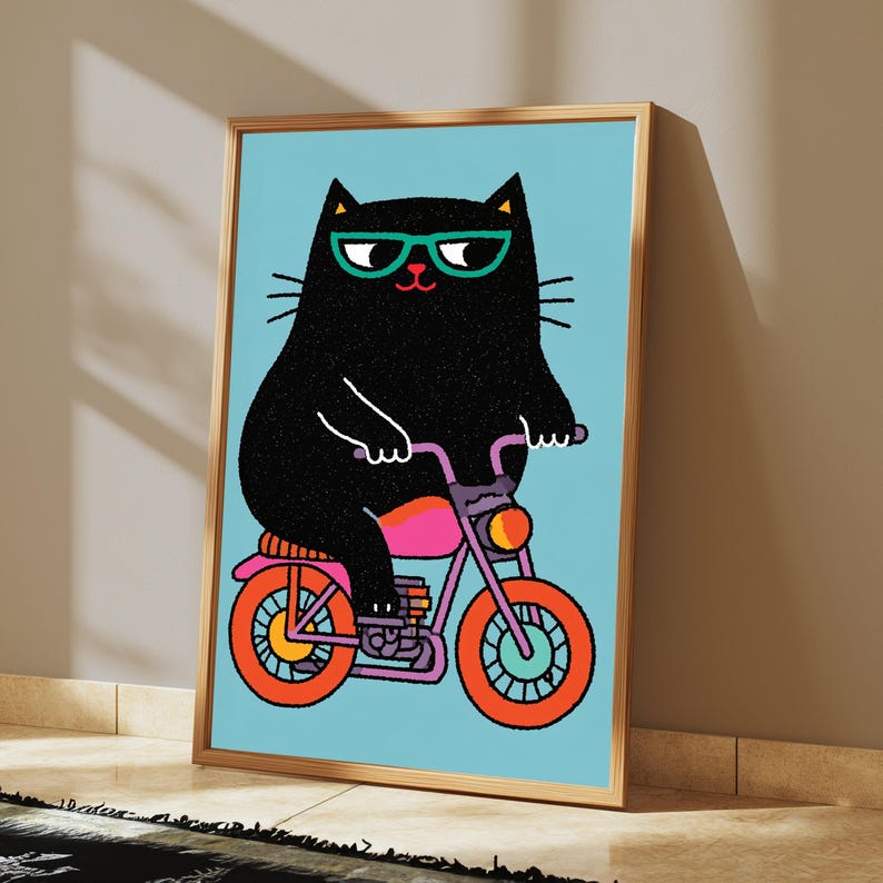 K&ouml;nnte beinhalten: Ein gerahmter Kunstdruck zeigt eine schwarze Katze mit t&uuml;rkisfarbener Brille auf einem rosa-violetten Motorrad mit orangefarbenen R&auml;dern vor hellblauem Hintergrund. Die Illustration verwendet kr&auml;ftige Linien und fl&auml;chige Farben f&uuml;r das Motiv.