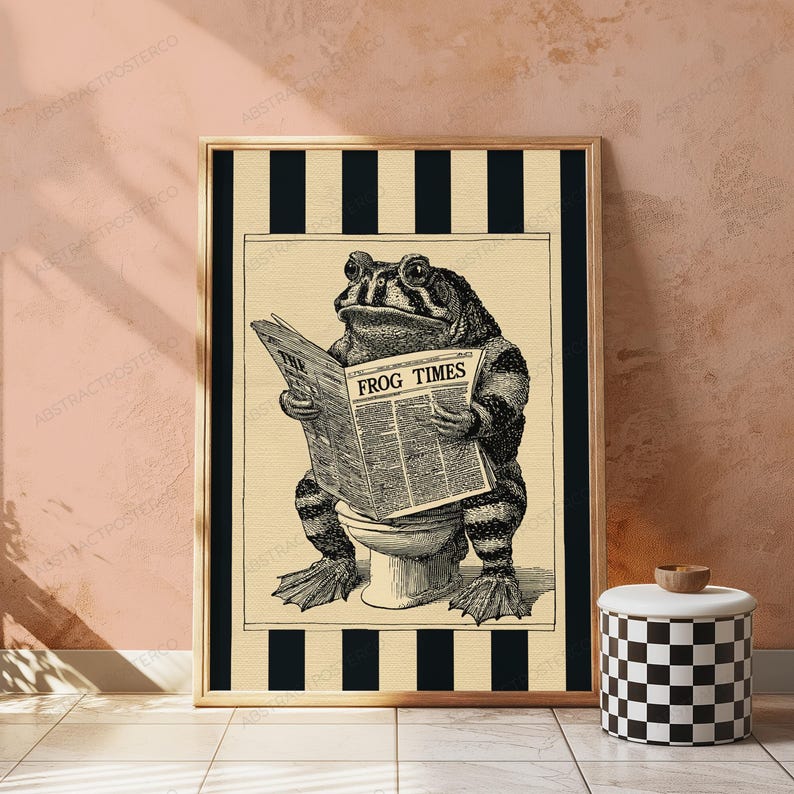 May include: A framed wall art print featuring a black and white illustration of a toad wearing glasses while sitting on a toilet and reading a newspaper titled THE FROG TIMES. The background consists of vertical black and white stripes.