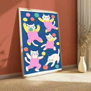 K&ouml;nnte beinhalten: Ein gerahmter vertikaler Kunstdruck mit f&uuml;nf wei&szlig;en Katzen mit rosa Wangen, die rosa Latzhosen tragen, vor einem texturierten dunkelblauen Hintergrund. Die Katzen sind in verschiedenen verspielten Posen dargestellt, umgeben von verstreuten bunten Kreisen in Gelb, Orange und Gr&uuml;n.