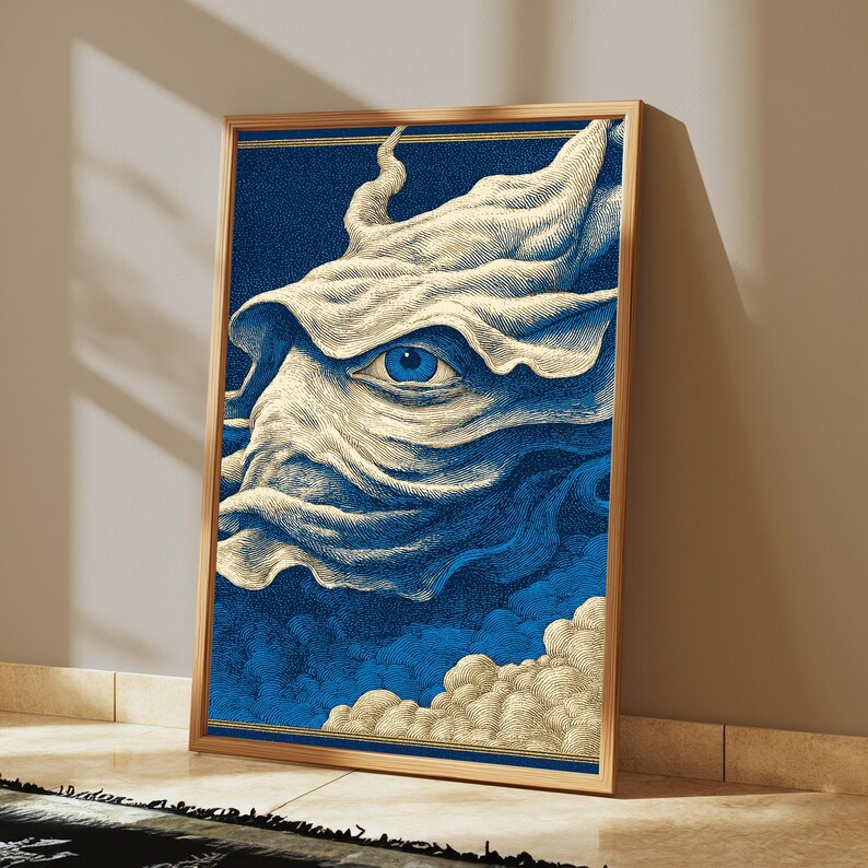 May include: A framed rectangular wall art print featuring a detailed illustration of a single blue eye centered within swirling, cream-colored fabric-like forms against a deep blue background, with clouds at the bottom and thin gold border lines.