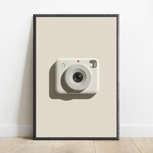 May include: A framed wall art print featuring a centered, off-white instant camera with a prominent circular lens, a small orange dot above the lens, and a rectangular viewfinder, set against a solid, light beige background within a black frame.