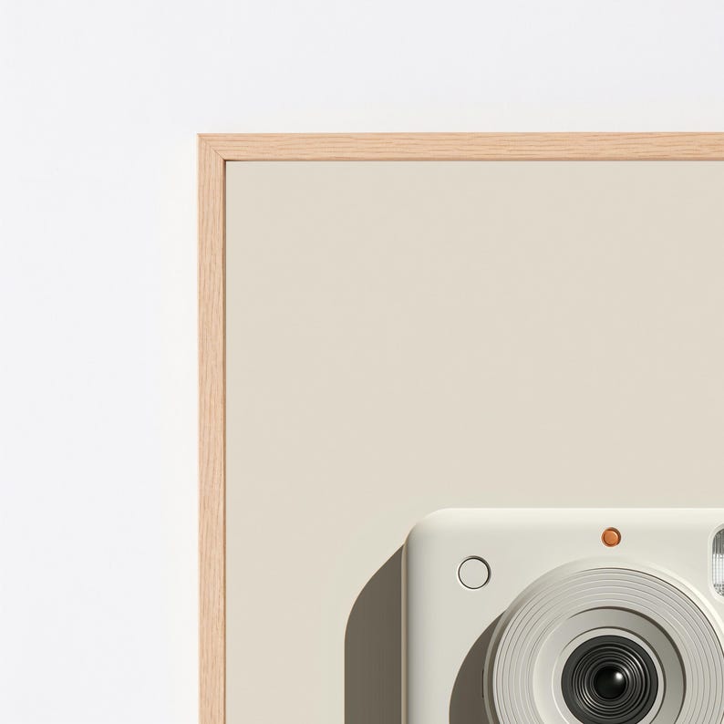 May include: A light beige instant camera with a circular lens, a small orange circular flash indicator, and a circular shutter button, framed within a light-colored wooden border against a plain, neutral-toned background surface.