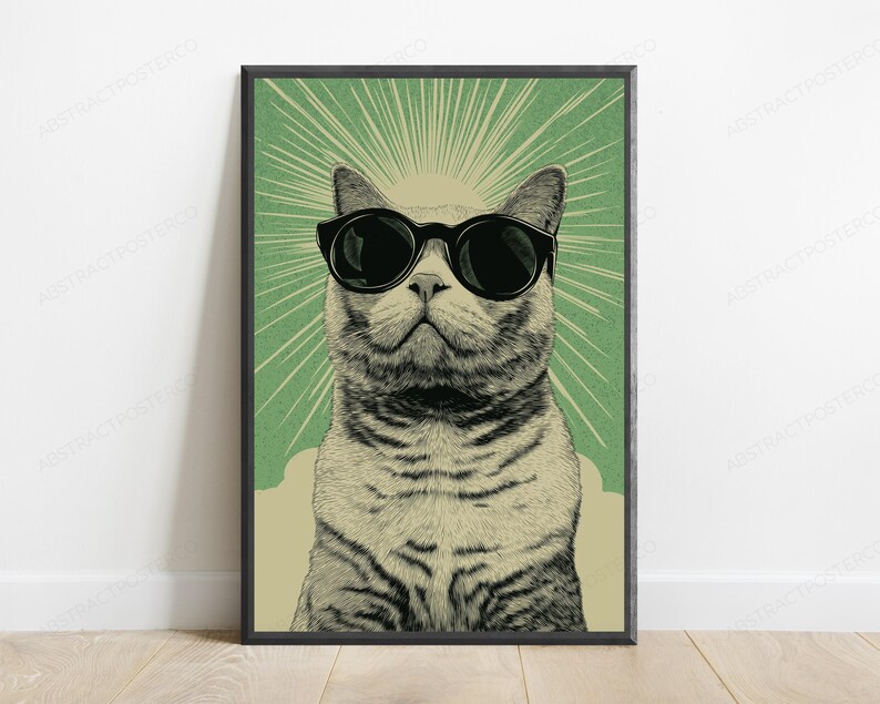 May include: A framed vertical wall art print featuring a detailed illustration of a cat wearing large black sunglasses. The cat is centered against a sage green background with radiating light lines emanating from behind its head in a sunburst pattern.