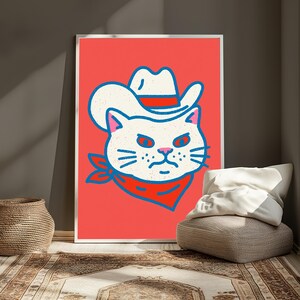 May include: A framed wall art print featuring a stylized illustration of a white cat wearing a white cowboy hat with a red band and a red bandana around its neck, set against a solid coral-red background with bold blue outlines.
