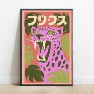 May include: A framed rectangular art print featuring a pink leopard with dark spots and green eyes, roaring with visible fangs. The background is a salmon-colored field with dark green tropical leaves and Japanese text at the top in cream.