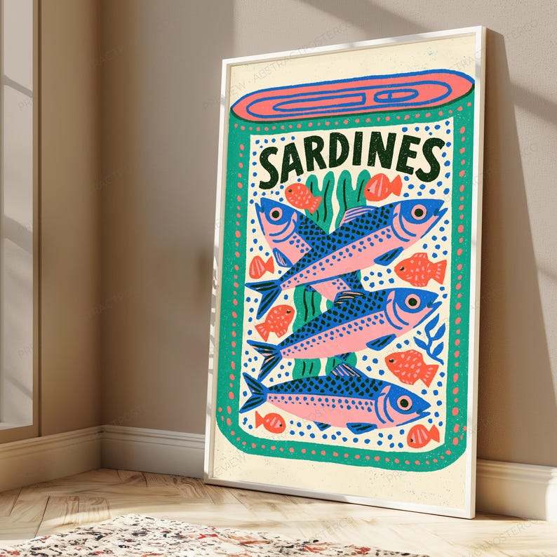 May include: A rectangular framed wall art print featuring a stylized illustration of a tin of sardines. The design includes the text SARDINES in dark green, three large blue and pink fish, and several smaller orange fish on a teal background.