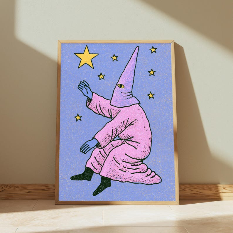 May include: A framed art print featuring a figure in a pink robe and a pointed hood with a single eye, reaching toward a large yellow star against a textured light blue background filled with smaller yellow stars. The print has a light wood frame.