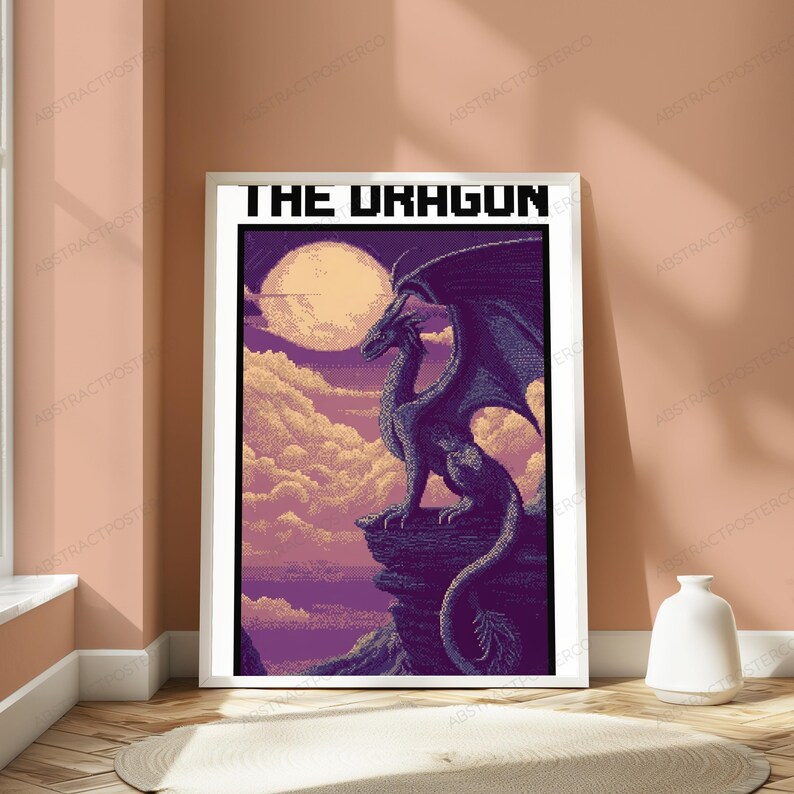 May include: A framed poster featuring pixel art of a dragon perched on a rocky cliff against a purple sky with a large moon and clouds. The text THE DRAGON is printed in a bold, black, blocky pixelated font at the top of the white-bordered print.