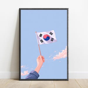 May include: A framed digital illustration featuring a hand holding a small South Korean flag against a light blue sky with soft pink clouds. The flag displays the central red and blue taegeuk symbol surrounded by four black trigrams on white.