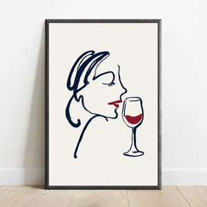 May include: A framed wall art print featuring a minimalist dark blue line drawing of a profile of a face with red lips, positioned next to a dark blue line drawing of a wine glass filled with red liquid, all set against a cream background.