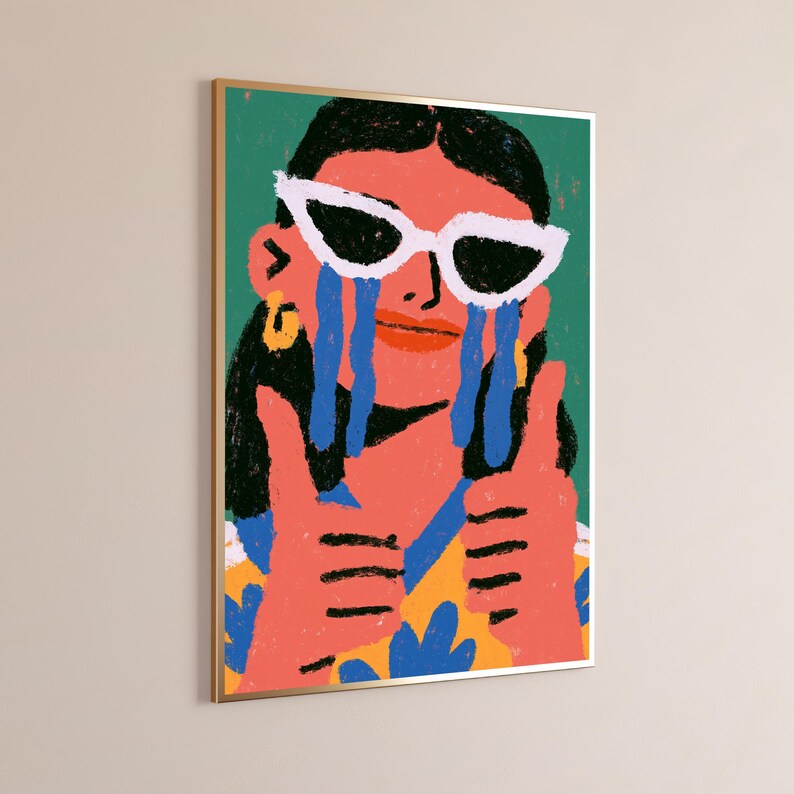 May include: A framed wall art print featuring a stylized illustration of a person with dark hair wearing white cat-eye sunglasses. The person has blue tears streaming down their face, is giving two thumbs up, and wears a yellow and blue patterned shirt.
