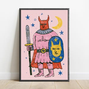 K&ouml;nnte beinhalten: Ein gerahmter Kunstdruck mit einer stilisierten Illustration einer geh&ouml;rnten Figur in einer rosa Tunika und einem Umhang, die ein graues Schwert und einen blauen Schild mit einem gelben Gesicht h&auml;lt. Der Hintergrund ist hellrosa mit gelbem Mond.