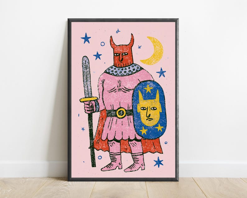 K&ouml;nnte beinhalten: Ein gerahmter Kunstdruck mit einer stilisierten Illustration einer geh&ouml;rnten Figur in einer rosa Tunika und einem Umhang, die ein graues Schwert und einen blauen Schild mit einem gelben Gesicht h&auml;lt. Der Hintergrund ist hellrosa mit gelbem Mond.