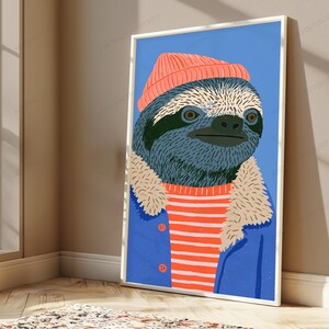 May include: A framed vertical art print featuring a stylized illustration of a sloth wearing a coral-colored beanie, a red and white striped shirt, and a blue jacket with a beige faux-fur collar, set against a solid light blue background.