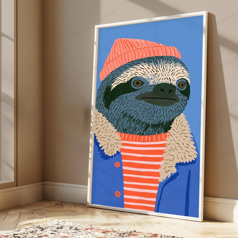 May include: A framed vertical art print featuring a stylized illustration of a sloth wearing a coral-colored beanie, a red and white striped shirt, and a blue jacket with a beige faux-fur collar, set against a solid light blue background.