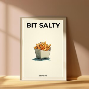 May include: A framed wall art print featuring a cream-colored background with the black text BIT SALTY at the top and standard at the bottom. In the center is a detailed illustration of golden-brown french fries in a white paper container.