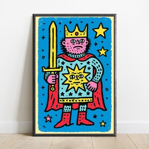 May include: A framed art print featuring a stylized illustration of a king with a pink face, wearing a yellow crown and a light blue tunic with a large yellow sun emblem. The figure holds a yellow sword, wears a red cape, and stands against a blue background with yellow stars.