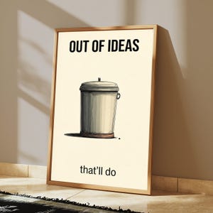 K&ouml;nnte beinhalten: Ein gerahmter Wandkunstdruck mit cremefarbenem Hintergrund und einer zentralen Illustration eines grauen M&uuml;lleimers mit Deckel. Der Text "OUT OF IDEAS" ist oben in Schwarz gedruckt, und der Text "that'll do" ist unten in Schwarz gedruckt.
