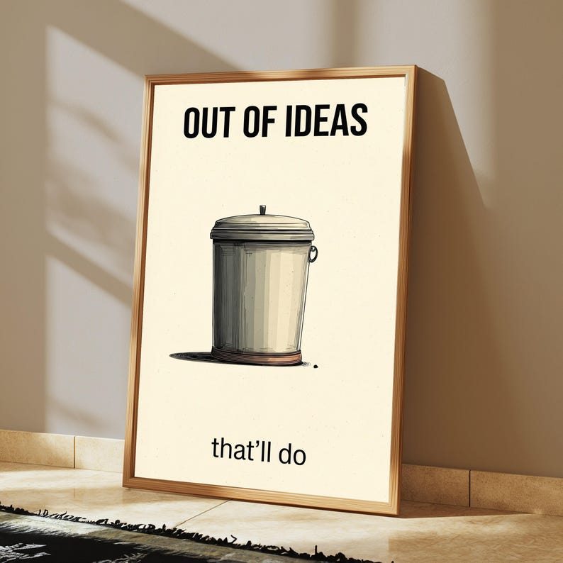 K&ouml;nnte beinhalten: Ein gerahmter Wandkunstdruck mit cremefarbenem Hintergrund und einer zentralen Illustration eines grauen M&uuml;lleimers mit Deckel. Der Text "OUT OF IDEAS" ist oben in Schwarz gedruckt, und der Text "that'll do" ist unten in Schwarz gedruckt.