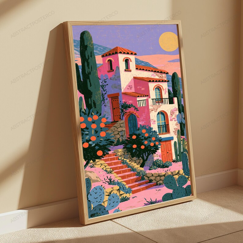 May include: A framed art print featuring a multi-story pink villa with arched windows and doors, surrounded by orange trees and cacti. A set of stone stairs leads up to the building under a purple sky with a large yellow sun in the background.