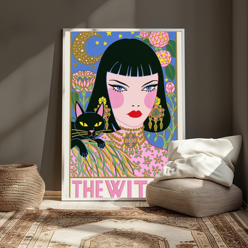 May include: A framed art print featuring a stylized illustration of a person with black hair, a black cat, and pink floral patterns against a blue background with a crescent moon. The text THE WITCH is printed in large pink letters at the bottom.