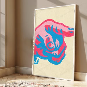 May include: A rectangular framed wall art print featuring a stylised graphic illustration of a hand pointing to the right. The design uses a vibrant colour palette of bright pink, hot pink, and electric blue against a textured cream background.