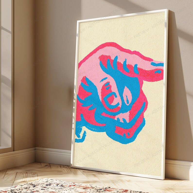 May include: A rectangular framed wall art print featuring a stylised graphic illustration of a hand pointing to the right. The design uses a vibrant colour palette of bright pink, hot pink, and electric blue against a textured cream background.