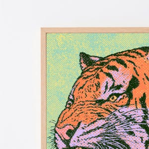 Może przedstawiać: Oprawiony wydruk ścienny przedstawiający stylizowaną głowę tygrysa z profilu. Grafika wykorzystuje żywą estetykę pop-art z wzorem kropek p&oacute;łtonowych, prezentując pomarańczowe, czarne, jasnofioletowe i miętowe kolory w jasnej drewnianej ramie.