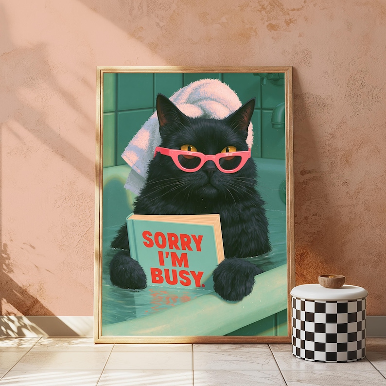 May include: A framed wall art print featuring a black cat in a bathtub wearing pink cat-eye glasses and a white towel on its head. The cat holds a light blue book with the red text SORRY I'M BUSY printed on the cover. The background shows green tiles.