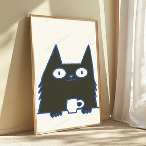 May include: A framed vertical wall art print featuring a stylized black cat with wide white eyes and a blue outline. The cat is positioned behind a white surface, holding a small white mug with both paws. The background of the print is off-white.