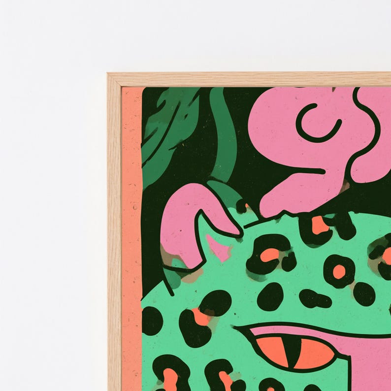 May include: A framed wall art print featuring a stylized green leopard with black spots, bright orange eyes, and pink accents against a dark background. The artwork is enclosed in a light-colored wooden frame with a thin, vertical peach-colored border.