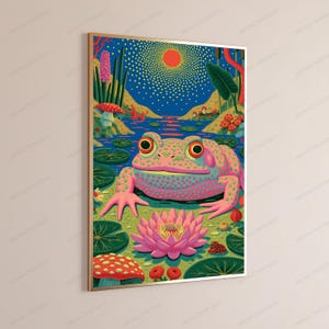 May include: A framed wall art print featuring a large, pink, spotted frog sitting in a pond. The scene includes a bright red sun in a dark blue sky, green lily pads, a blooming pink lotus flower, and red-capped mushrooms in a vibrant landscape.