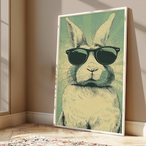 May include: A framed vertical wall art print featuring a detailed illustration of a rabbit wearing black sunglasses. The rabbit is centered against a light green background with radiating sunburst lines in a darker shade of green.
