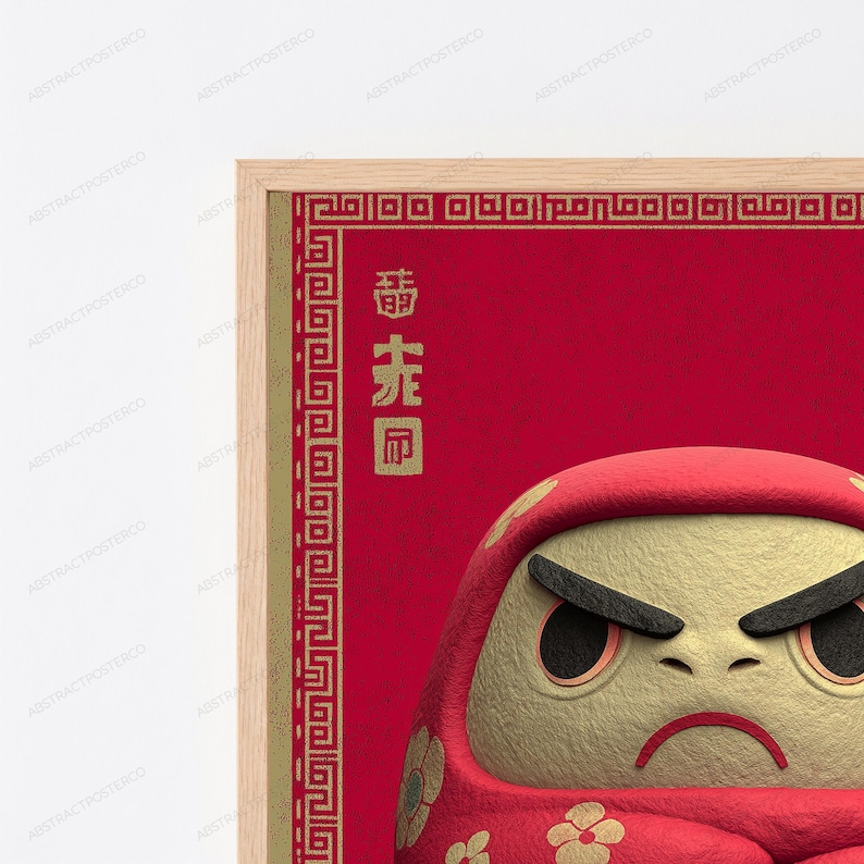 Peut inclure: Une affiche encadr&eacute;e repr&eacute;sentant une poup&eacute;e Daruma rouge avec un visage beige textur&eacute;, des sourcils et des yeux noirs. Le fond est rouge profond avec une bordure g&eacute;om&eacute;trique dor&eacute;e et des caract&egrave;res chinois verticaux en police dor&eacute;e.