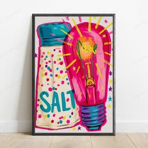 May include: A framed art print featuring a white salt shaker with a blue cap and colorful confetti dots, labeled with the word SALT in blue. Next to it is a bright pink light bulb with yellow rays and small stars, all in a vibrant pop art style.