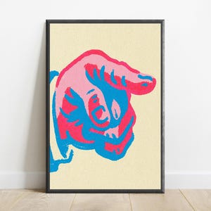 May include: A framed wall art print featuring a stylised graphic of a hand pointing to the right. The design uses a bold colour palette of bright pink and vibrant blue against a textured, pale cream-coloured background within a thin black frame.