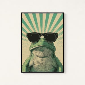 K&ouml;nnte beinhalten: Ein gerahmter Wandkunstdruck, der einen gr&uuml;nen Frosch mit einer schwarzen Sonnenbrille zeigt. Der Hintergrund besteht aus einem beigen und blaugr&uuml;nen Sonnenstrahlenmuster mit einer gepunkteten Textur. Der Frosch ist mittig platziert.