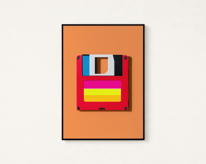 May include: A framed wall art print featuring a red floppy disk centred on a solid orange background. The disk has a white sliding metal shutter, a blue and black top section, and a label with horizontal pink, yellow, and orange stripes.