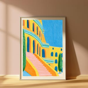 May include: A framed art print featuring a vibrant illustration of a yellow building with arched blue doorways, a pink staircase, and two tall green cypress trees against a bright blue sky. The artwork uses visible brushstrokes and bold colours.