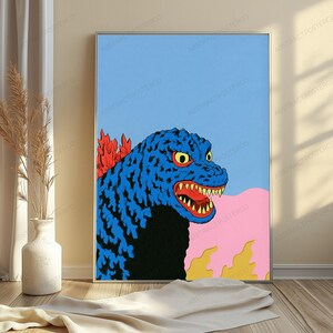 May include: A framed art print featuring a stylised blue monster with yellow eyes and sharp teeth, set against a light blue sky. The creature has red dorsal fins and is positioned above a pink landscape with yellow flame-like shapes at the bottom.