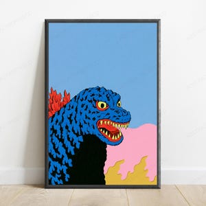 May include: A framed wall art print featuring a stylised blue monster with yellow eyes and sharp teeth. The creature has red dorsal fins and is positioned against a light blue sky, with a pink cloud and yellow flames visible at the bottom.
