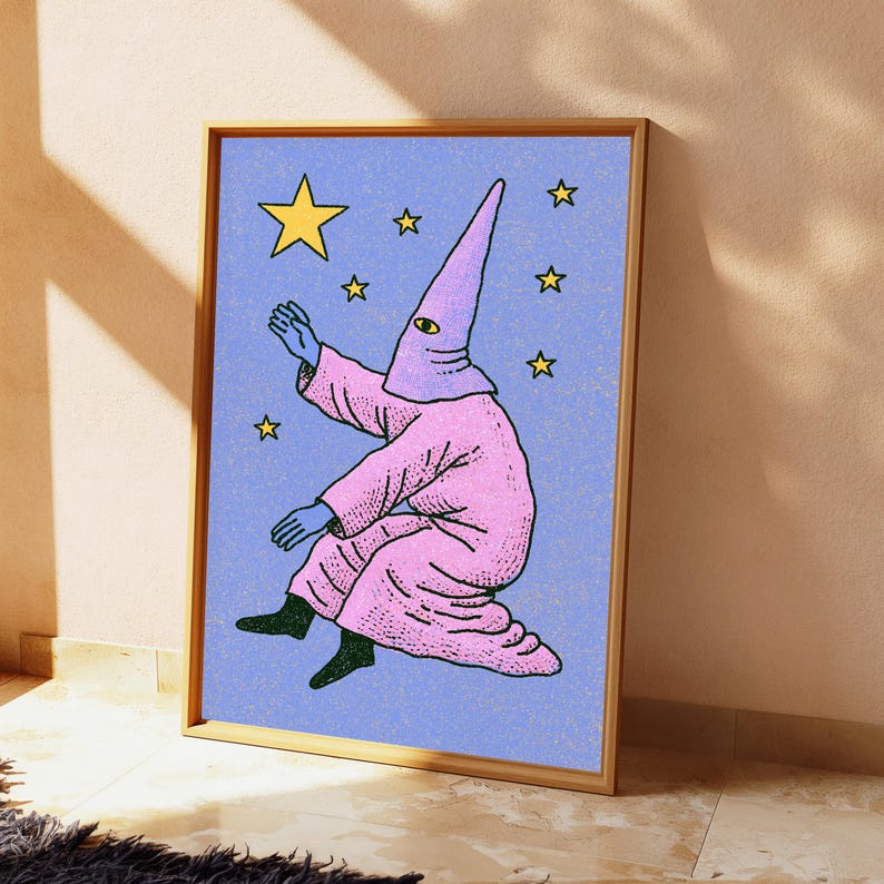 May include: A framed art print featuring a figure in a pink hooded robe with a single visible eye, reaching toward yellow stars against a textured light blue background. The figure has blue hands and dark feet, rendered in a graphic illustration style.