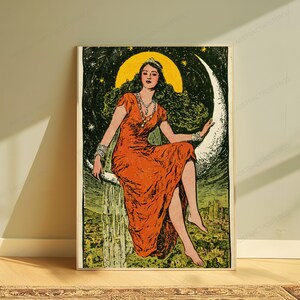 May include: A vertical art print featuring a person with long dark hair wearing a long orange dress, seated on a large white crescent moon against a dark green starry sky. Below the moon, a landscape with buildings is visible in a muted green tone.