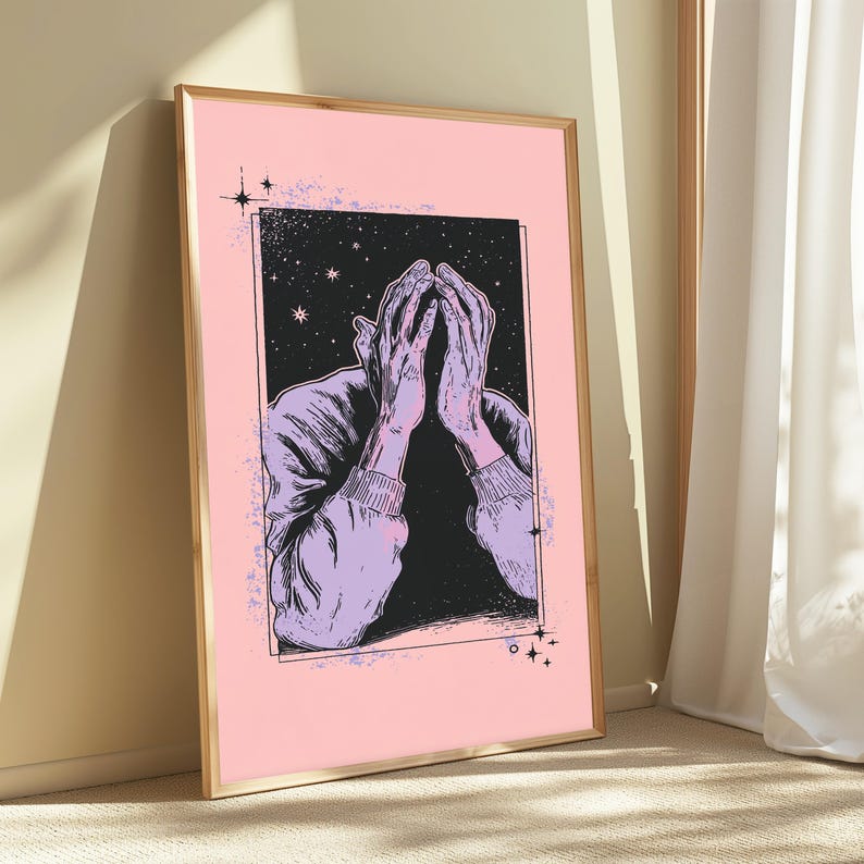 May include: A framed rectangular wall art print featuring a light pink background and a central black rectangular panel. The illustration depicts two hands held up to a face, rendered in light purple with black line work, set against a starry night sky.