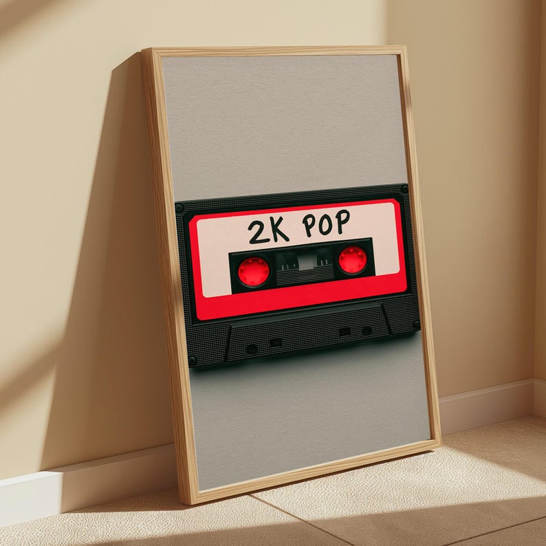 May include: A framed vertical wall art print featuring a black and red cassette tape graphic centred on a light grey background. The cassette tape has a white label area with the text 2K POP written in black, and two bright red circular spools.