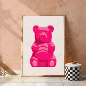 May include: A framed wall art print featuring a centered, solid hot pink gummy bear illustration on a plain white background. The artwork is enclosed in a thin, light-colored wooden frame, displaying a clean and simple graphic design.