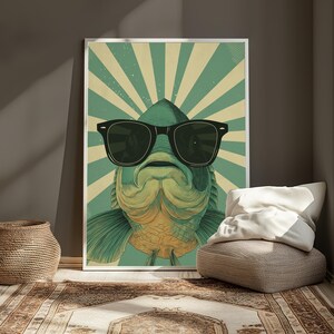 May include: A framed wall art print featuring a stylised illustration of a green fish wearing large black sunglasses. The background consists of a radiating sunburst pattern in alternating shades of light green and cream, creating a bold graphic design.