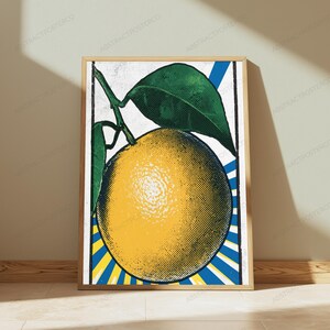 May include: A framed vertical art print featuring a stylized yellow orange with green leaves. The design uses a halftone dot pattern against a background of radiating blue and yellow stripes, enclosed within a thin black border frame.