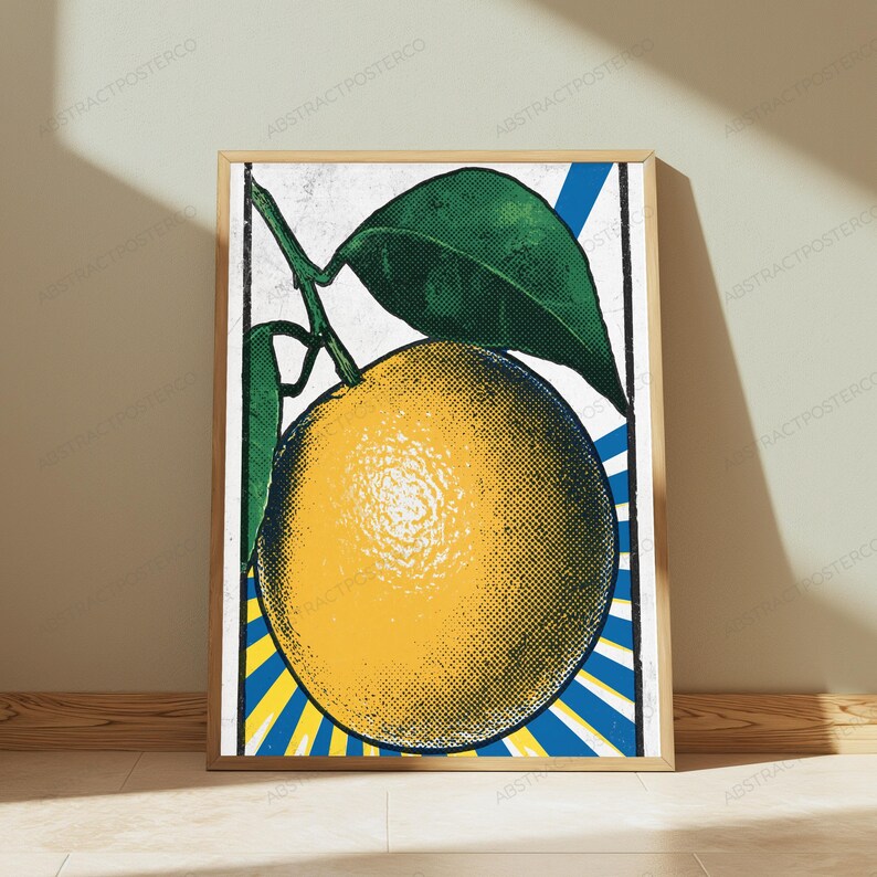 May include: A framed vertical art print featuring a stylized yellow orange with green leaves. The design uses a halftone dot pattern against a background of radiating blue and yellow stripes, enclosed within a thin black border frame.